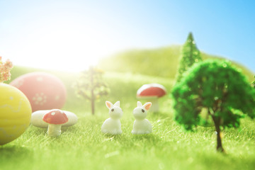 Easter rabbits toys with easter eggs on green grass. Fairy tale sunset on the green field with grass, mushrooms and trees. Macro.