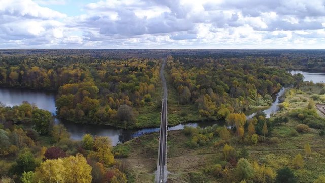 Flying over the railway in the early autumn beautiful forest and over the small river in the cloudly day.
