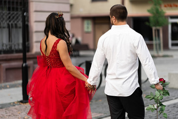 Beautiful romantic couple. Attractive young woman in red dress and crown with handsome man in white shirt with red rose back view.Happy Saint Valentine's Day. Pregnant and wedding concept.