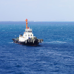  White towing ship in the ocean. A floating tow boat against a background of blue water and a clear...