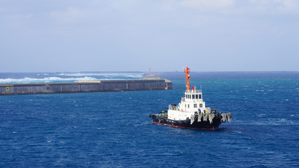  White towing ship in the ocean. A floating tow boat against a background of blue water and a clear...