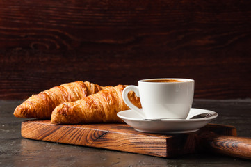 Espresso in a white cup and two croissants on dark background, on a wooden board, place for text, side view