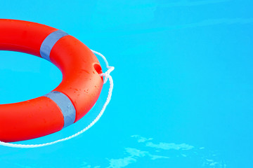 Orange lifebuoy pool ring float on blue water. Life ring in swimming pool. Copyspace.