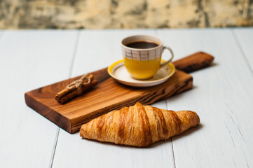 Tasty croissant and sweet coffee in yellow cup with cinnamon on a light background
