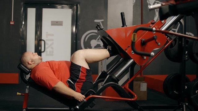 overweight man doing exercise on leg press trainer at the gym. male working out to lose weight. concept of goal, hardwork, obesity, fat, weightlifting, body, push, training.