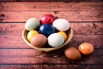 Raw eggs and color easter eggs on wooden table, in basket.