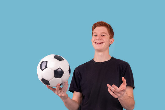 Shot of a red-haired teenager holding a soccer ball in his hand on a blue background.