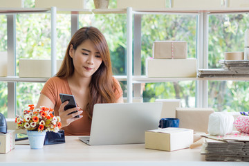 Beautiful Asian businesswoman holding a smartphone and looking at a laptop while sitting in the office