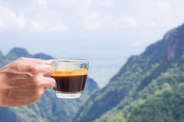 Close-up of a man hand holding a coffee cup with beautiful scenery view of mountains. Morning coffee feeling happy and freedom. Space for text