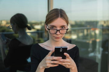Young business woman uses phone. Good looking brunette female uses online banking on smart phone to transfer money from credit card. Girl using smart phone and chatting with business partners.