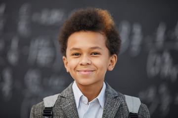 Portrait of African schoolboy with backpack behind his back smiling at camera at school