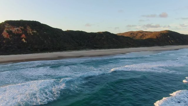 Beautiful high angle aerial drone footage of famous Seventy Five Mile Beach near Dundubara Creek on Fraser Island, Queensland, Australia, shortly before sunset. Mist over the forest.