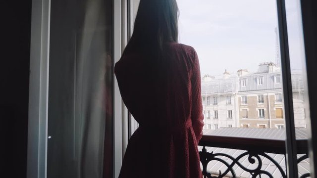 Rear view of beautiful happy female tourist standing at room balcony watching romantic Eiffel Tower view slow motion.