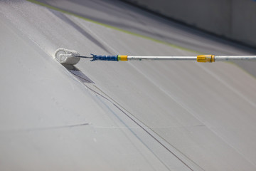 Painting a large surface white with a paint roller on a stick.