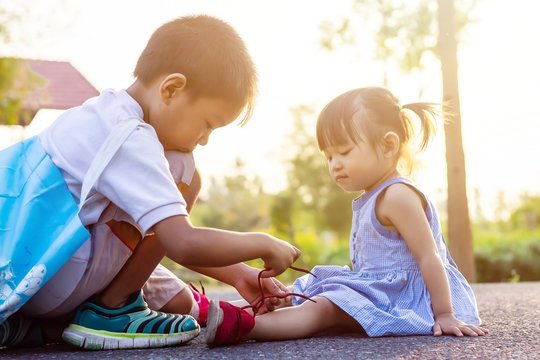Soft focus. A young Asian brother help his little sister to tie her shoelaces. At the garden park in sunshine day summer season. Love and family concept.