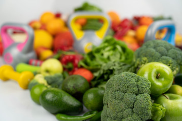 Fitness concept. Healthy nutrition: fruits and vegetables. Equipment for fitness exercises: weighing machine and dumbells. White background.