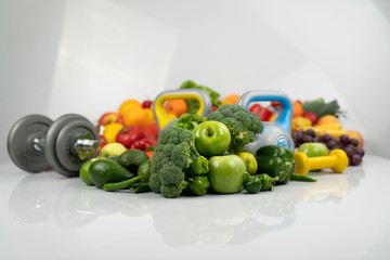 Fitness concept. Healthy nutrition: fruits and vegetables. Equipment for fitness exercises: weighing machine and dumbells. White background.