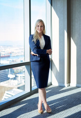 Obraz premium Confident young businesswoman standing by office windows overlooking the city