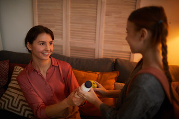 Smiling young mother sitting on sofa and giving a lunch to her daughter to school