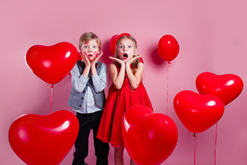 Surprised little boy with red kisses on the skin and girl in red balloons on pink background