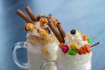 Two glasses or jars of freak shakes on rustic wooden table. Caramel marshmallow candy milk shake cocktail.