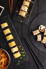 Traditional Asian cuisine sushi rolls and noodles on a black wooden table