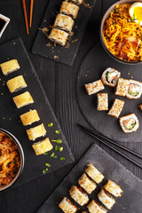 Traditional Asian cuisine sushi rolls and noodles on a black wooden table