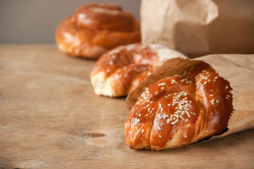 Fresh pastry with sesame seeds packed in paper on wooden table. Bakery products. Selective focus. Space for text.
