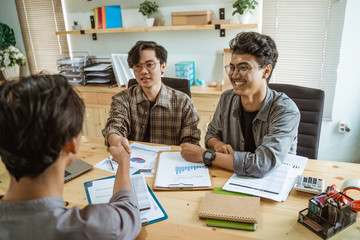 three young Asian business people shook their hands in agreement on a production plan at meeting