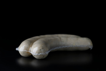 Two long white raw bratwurst sausage in plastic wrap isolated on black background