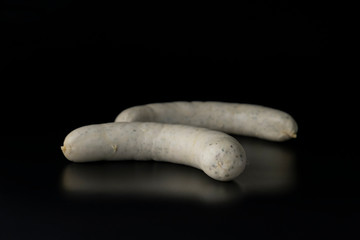 Two long white raw bratwurst sausage isolated on black background