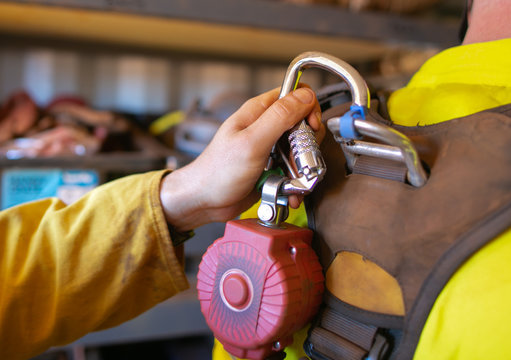 Close up construction hand clipping locking carabiner which connecting into self retractable shock absorber safety device equipment rope access body harness rescue loop prior work