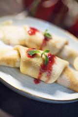 delicious crepes desert with red strawberry sauce, honey and green on white plate served with spoon