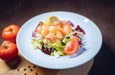 Salmon salad with lettuce, lemon, spices, seeds closeup in white plate
