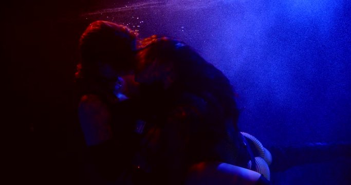 Two fateful sexy girls with long hair are in the Studio under water on a blue background. They are lesbians hugging and kissing. Their hair is flying. They wear short tops and shorts.