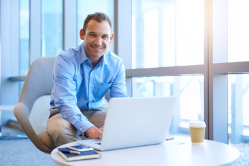 Middle-aged businessman smiling confidently in bright office with laptop