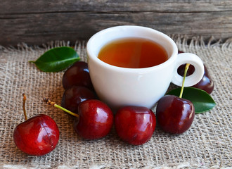 Cherry fruit tea with freshly picked cherries in a white cup on a burlap cloth.Selective focus