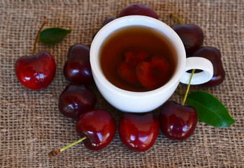 Cherry fruit tea with freshly picked cherries in a white cup on a burlap cloth.Selective focus