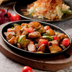 Delicious oven-baked potatoes with herbs and vegetables in a pan, rustic style. Potatoes fried, red cherry tomato, zucchini, onion on gray stone background.