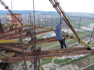 Athlete man hanging an iron rail on top of a tall industrial chimney with the risk of falling to his death hundred meters from the ground