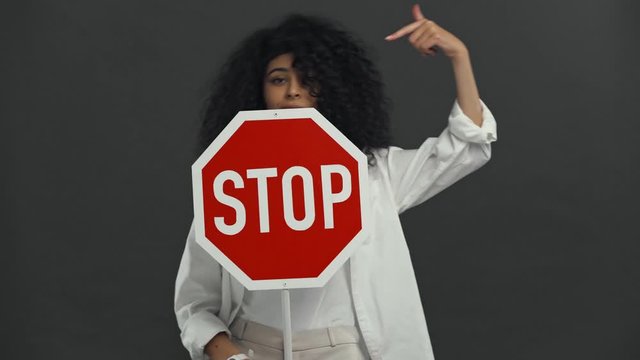 skeptical bi-racial woman holding stop placard isolated on black