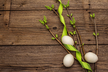 Zero waste Easter concept. Spring twigs with fresh green leaves, wooden eggs, polka dot ribbon. Old vintage wooden boards background