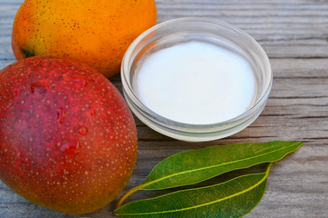 Mango body butter in a glass bowl and fresh ripe mangoes fruit on old wooden table.Spa,organic cosmetic or healthcare concept.Selective focus.