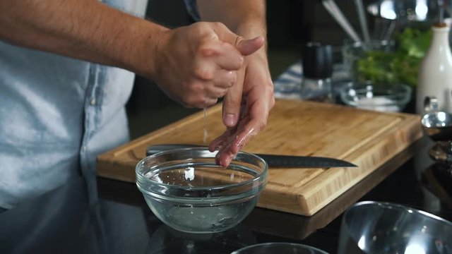 Close-up of cook’s hands, man crushes lime with his hands, juice drips into bowl, shot in studio, preparing sauce, lime juice we use as ingredient for sauce, squeeze fruit, professional cook