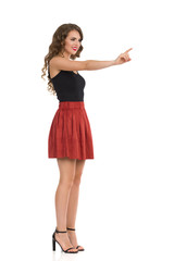 Young Woman In Brown Suede Mini Skirt And High Heels Is Pushing Something With Index Finger. Side View.