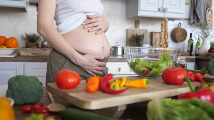 Closeup Of Pregnant Woman Holding Her Belly While Cooking Healthy Meal.