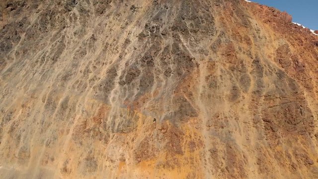 Aerial reveal shot of Mount Ushba, Georgia, starting with a view of a rocky wall in front of the mountains.