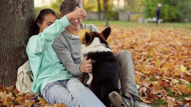 Happy Loving Couple making selfie on smartphone with cute tricolor Welsh Corgi Dog In City Park hugging relaxing enjoying warm day outdoors. People and animals concept.