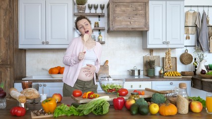 Happy Pregnancy Concept. Cheerful Pregnant Girl Dancing And Singing In Kitchen.