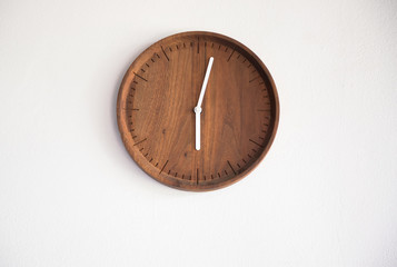 wooden clock wall on white concrete panel. time at 6 A.M. in morning.